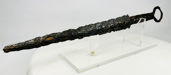 Medieval European dagger with ring pommel and corroded forged steel blade on acrylic display stand — 14th-century weapon artifact photographed on white background.