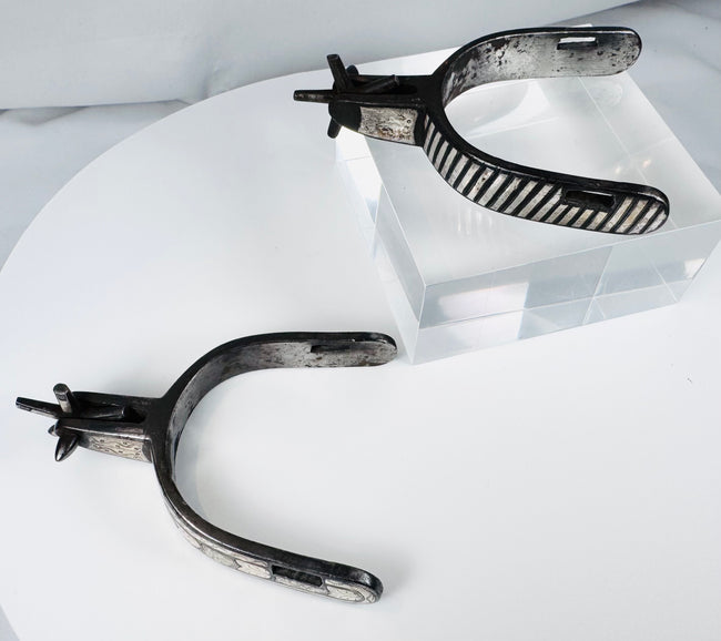 Decorated steel cowboy spurs with silver overlays, strap slots, and aged surface