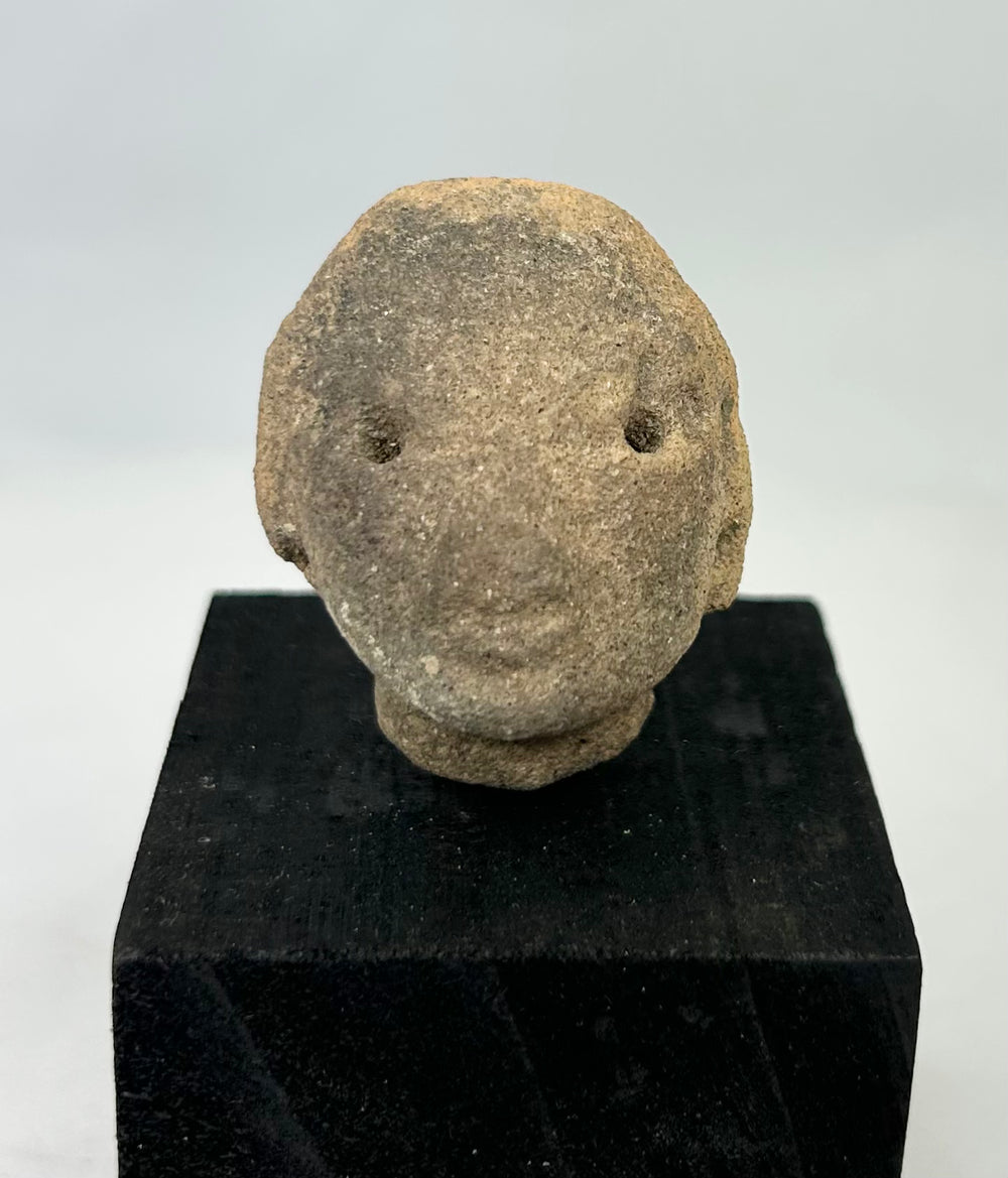 West Mexican Pre-Columbian terracotta head fragment, circa 300 BCE–300 CE, featuring drilled eyes and gentle facial features on a display stand