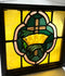 Wood-framed stained glass panel from early 20th century, featuring central cross and crown motif in amber, green, and pink, 16 inches square.