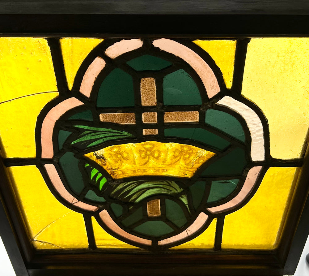 Close view of Early 20th-century 16x16 in. stained glass panel with amber, green, and pink cross and crown motif in wooden frame.