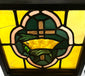 Close view of Early 20th-century 16x16 in. stained glass panel with amber, green, and pink cross and crown motif in wooden frame.