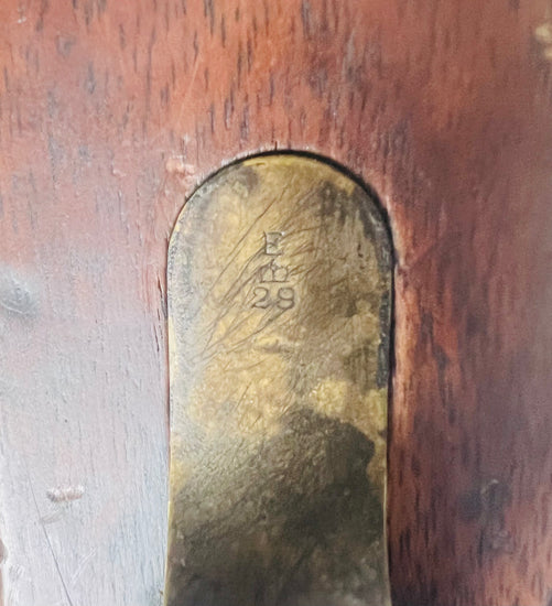 Close-up of engraved brass unit mark inset into the wooden stock of a Victorian-era Snider-Enfield rifle.