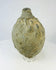 Angled view of an Islamic ceramic hand grenade from Greater Persia, 10th–12th century CE, displaying its textured surface, globular body, and aged patina on a white background.