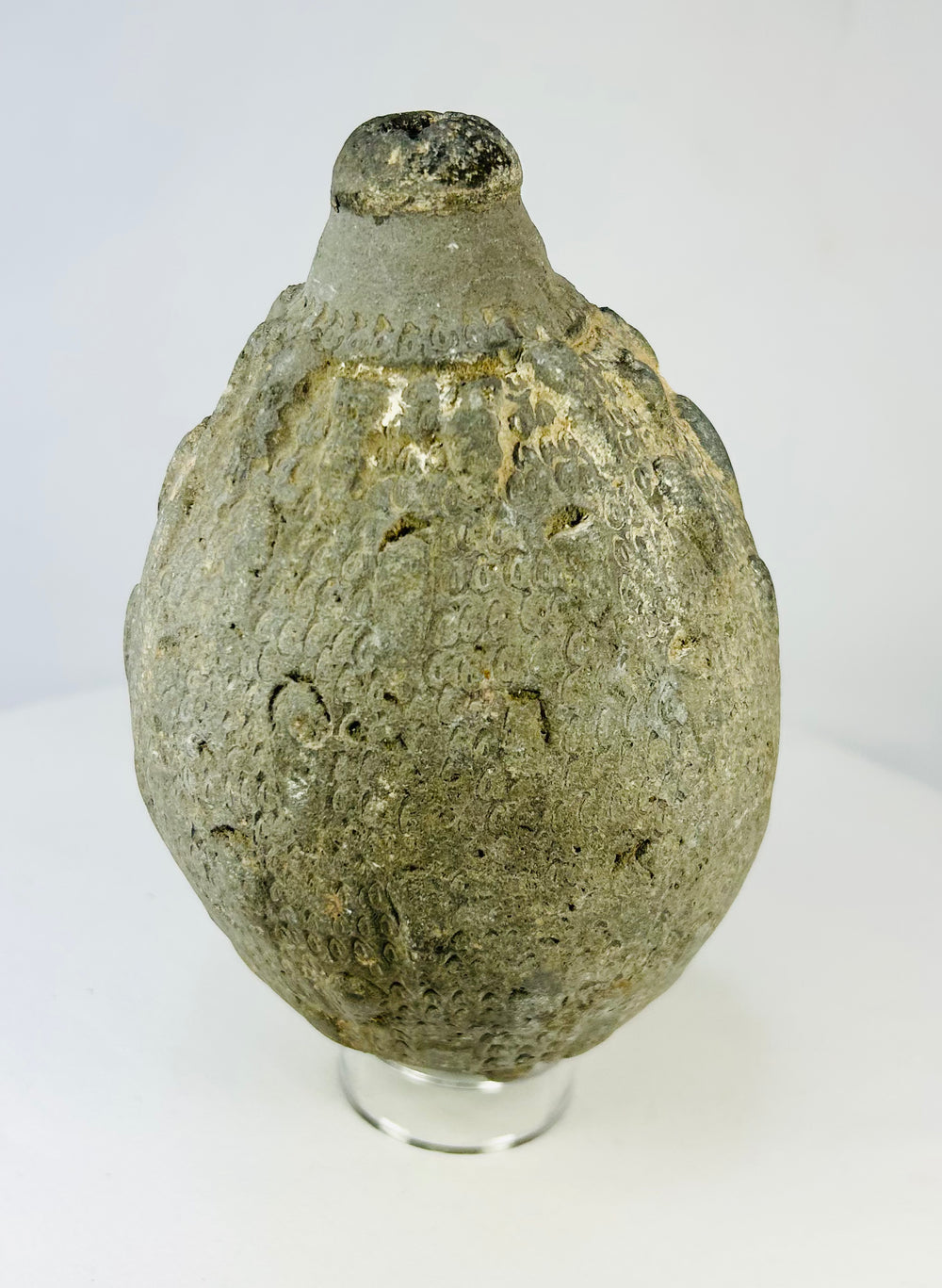Side view of an Islamic ceramic hand grenade from Greater Persia, 10th–12th century CE, displaying its textured surface, globular body, and aged patina on a white background.