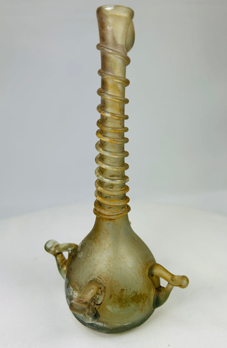 Side profile of ancient Middle Eastern glass vessel with tall neck, rounded base, and slight weathering from age.