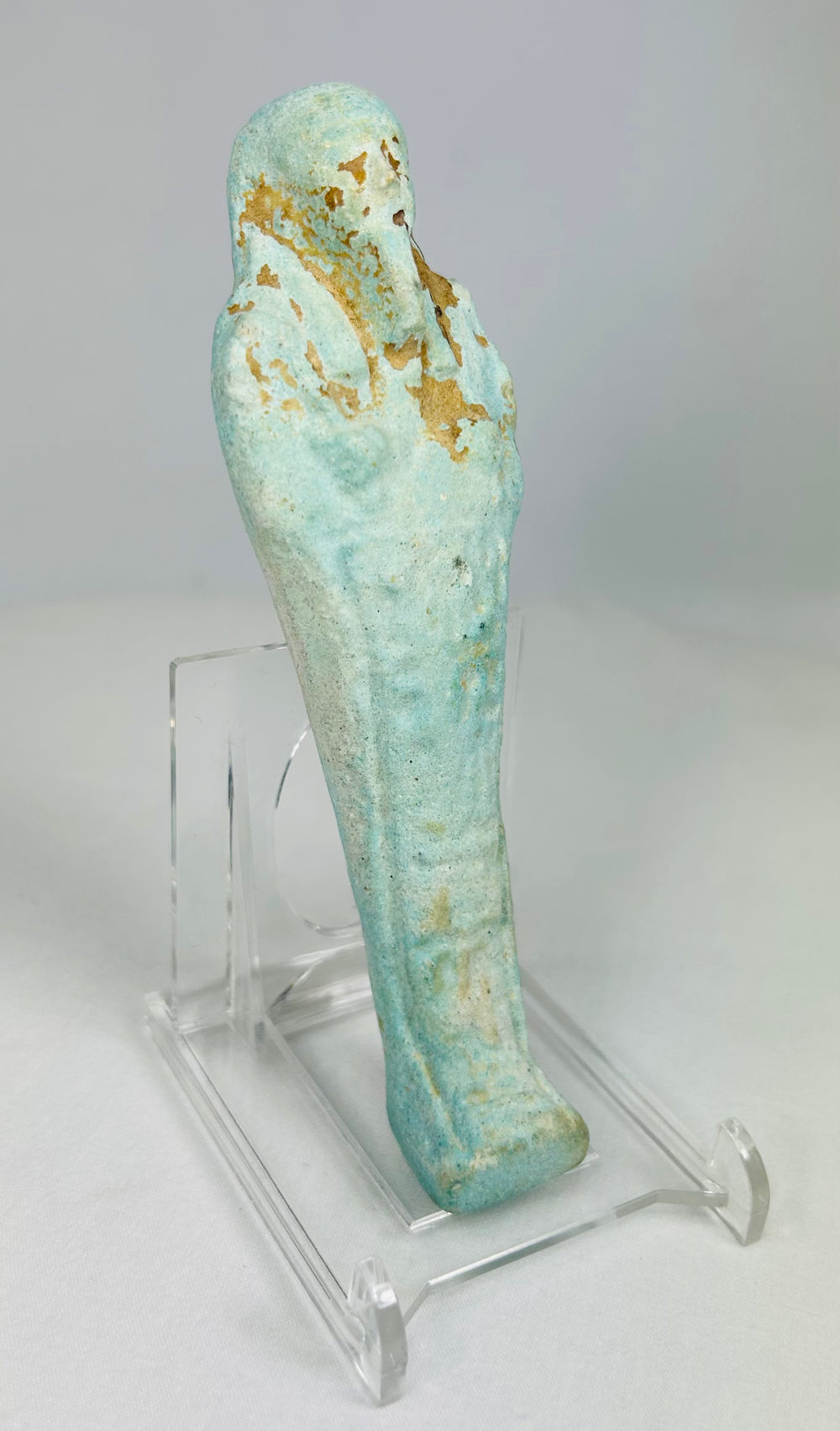 Slight right angle of blue-glazed Egyptian ushabti with crossed arms and agricultural implements.