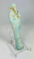 Slight right angle of blue-glazed Egyptian ushabti with crossed arms and agricultural implements.