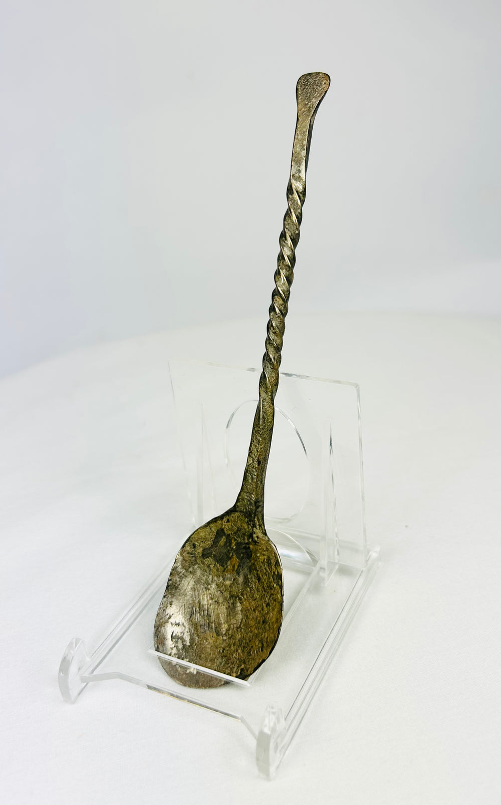 Slight left view of ancient bronze spoon with twisted stem and encrusted green patina.