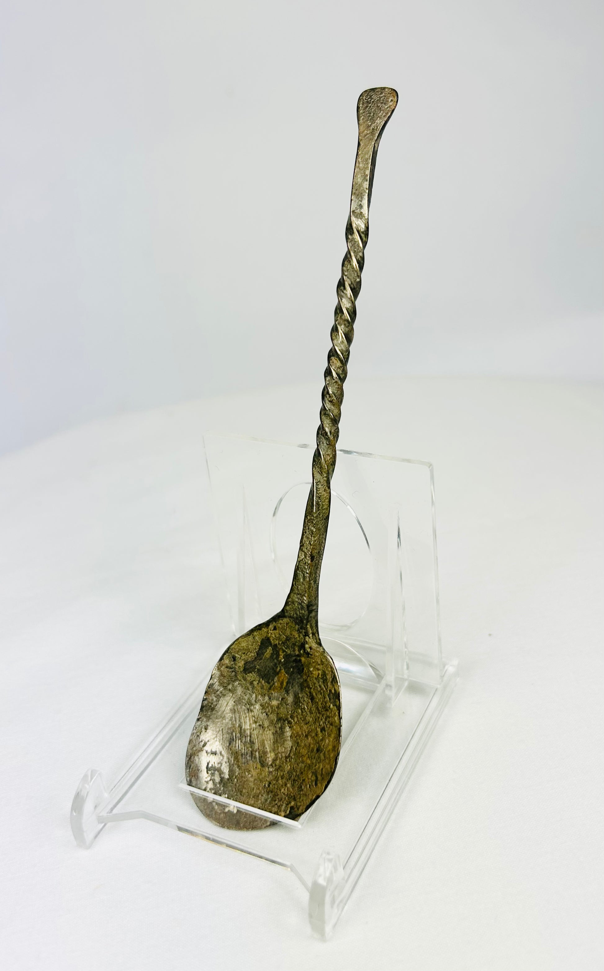 Slight left view of ancient bronze spoon with twisted stem and encrusted green patina.