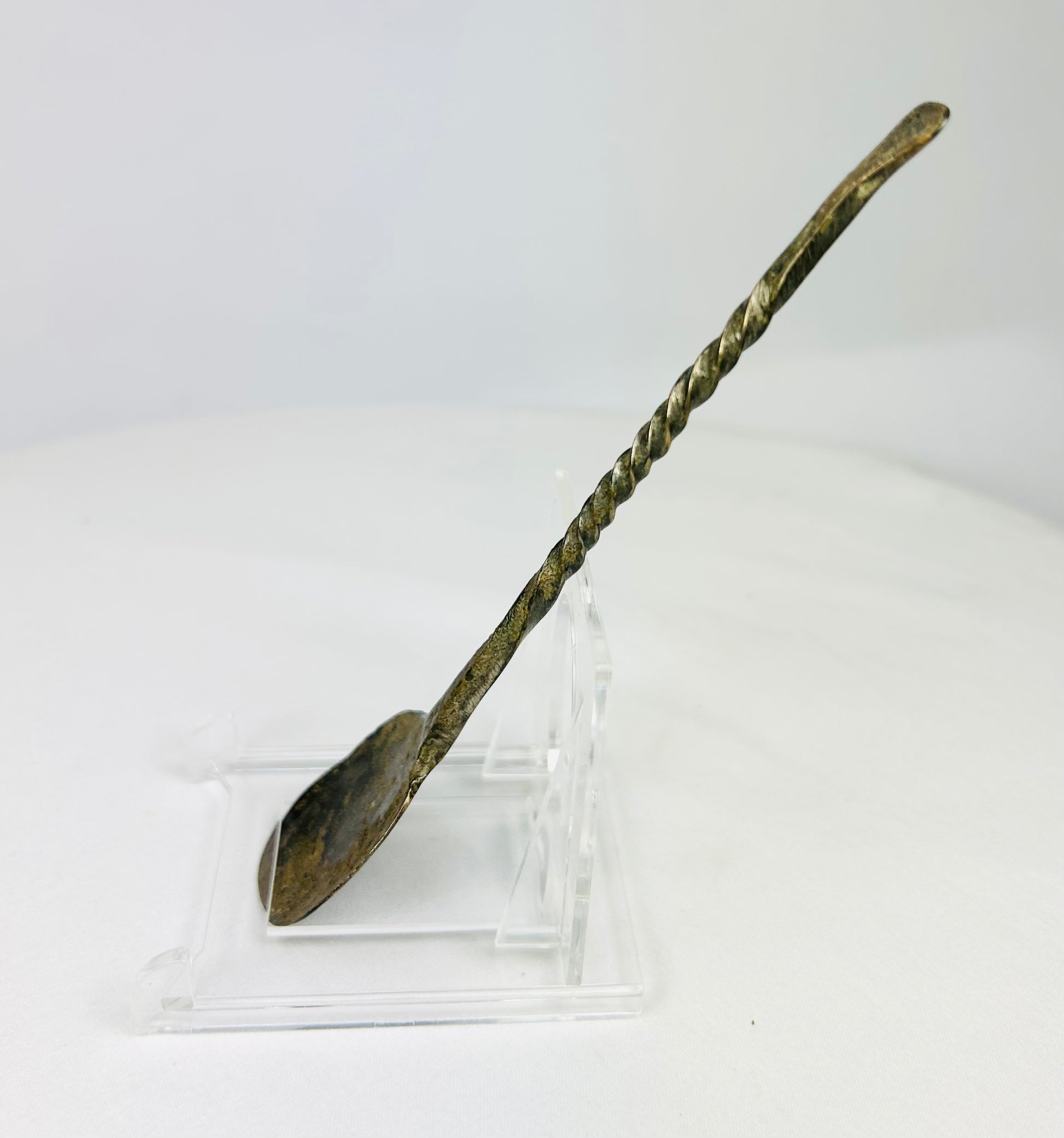 Left side profile of ancient bronze spoon highlighting elegant spiral handle design and encrusted surface texture.