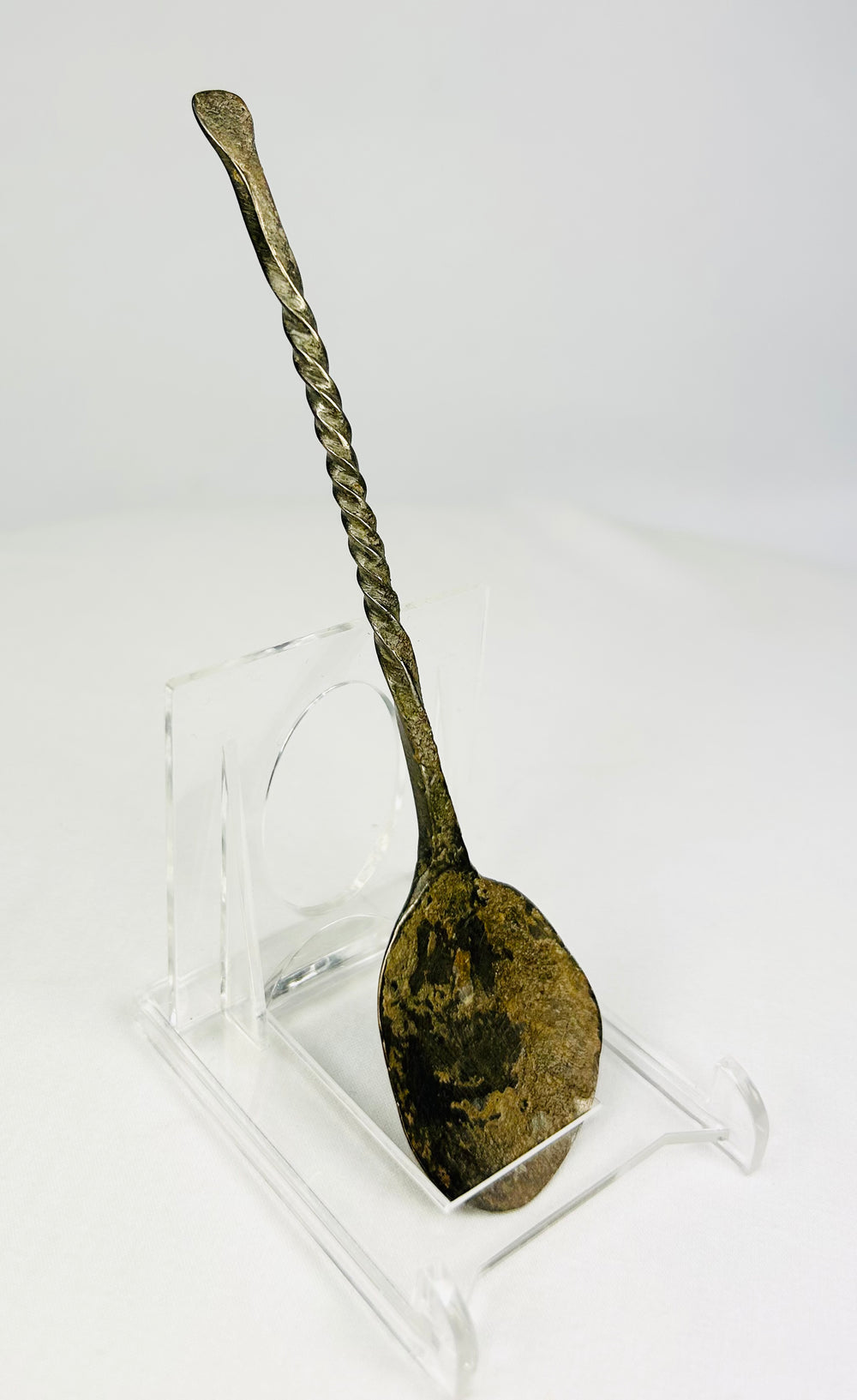 Forward-tilted view of ancient bronze spoon revealing curvature of handle and weathered metal finish.
