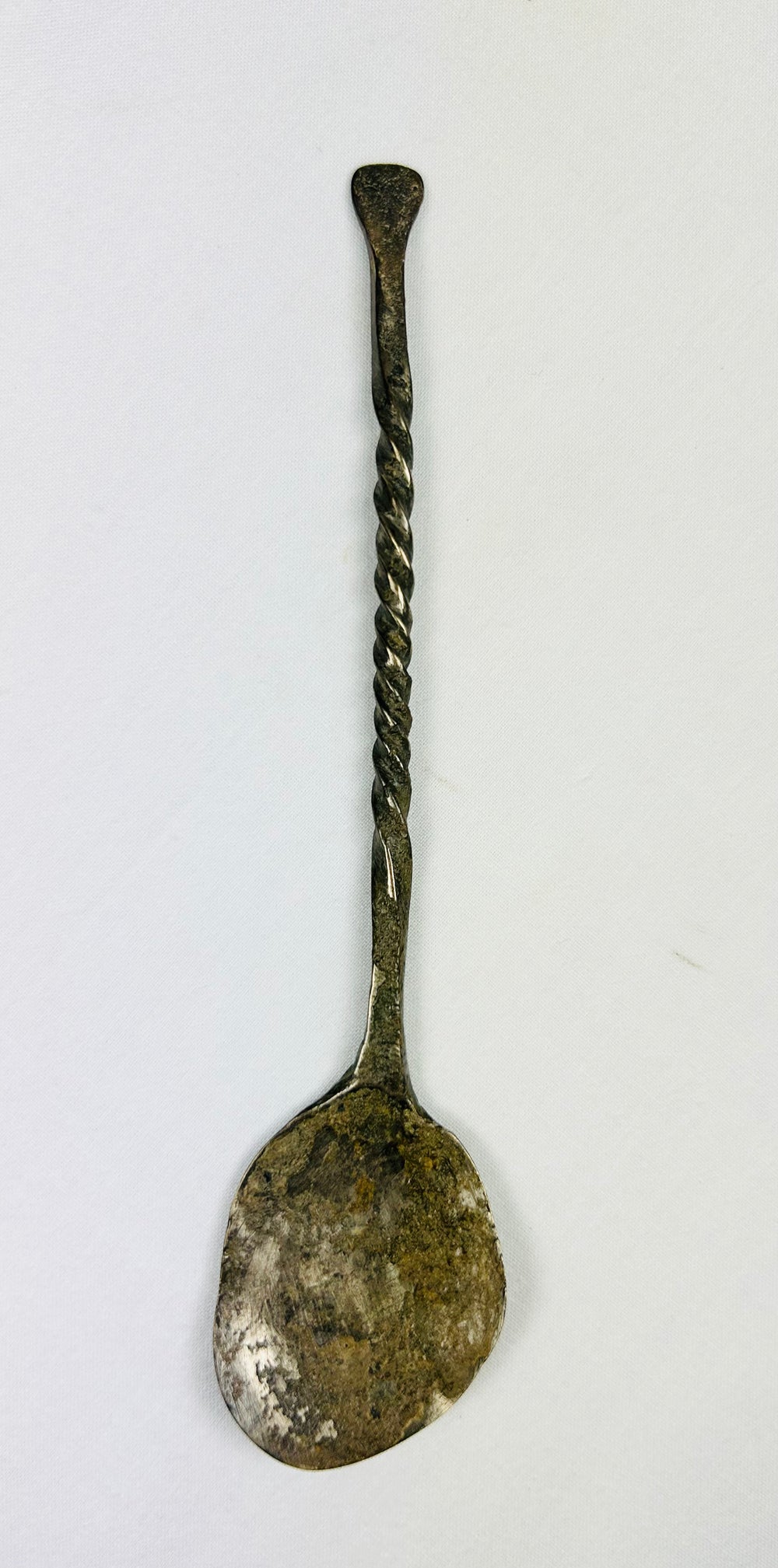 Top-down view of ancient bronze spoon with narrow handle and circular bowl, aged bronze patina.