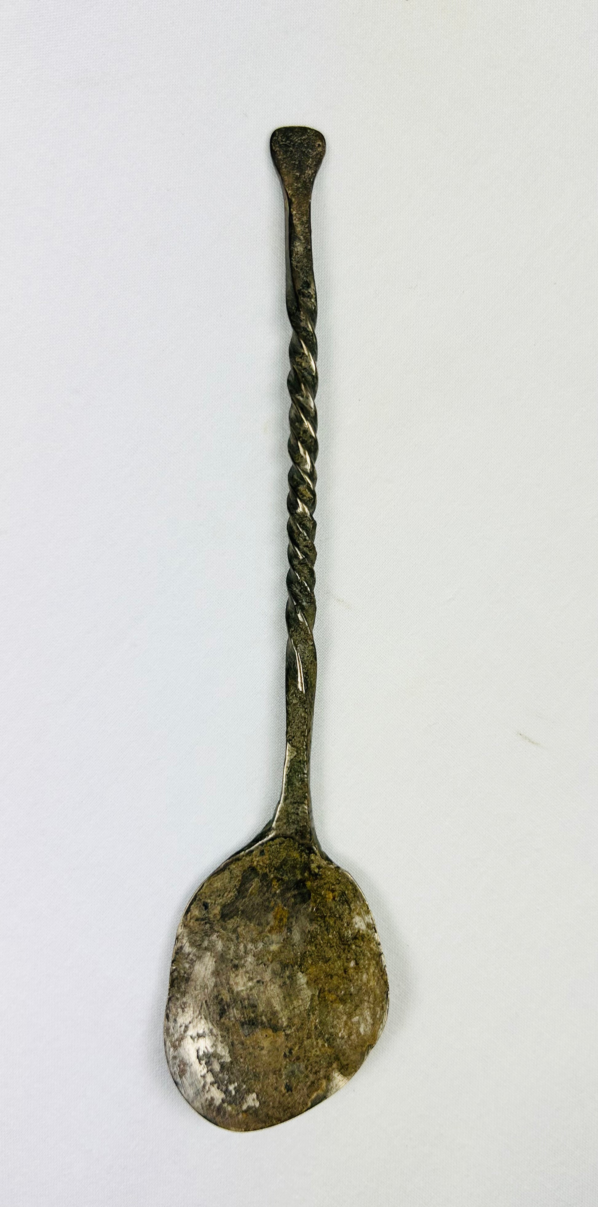 Top-down view of ancient bronze spoon with narrow handle and circular bowl, aged bronze patina.