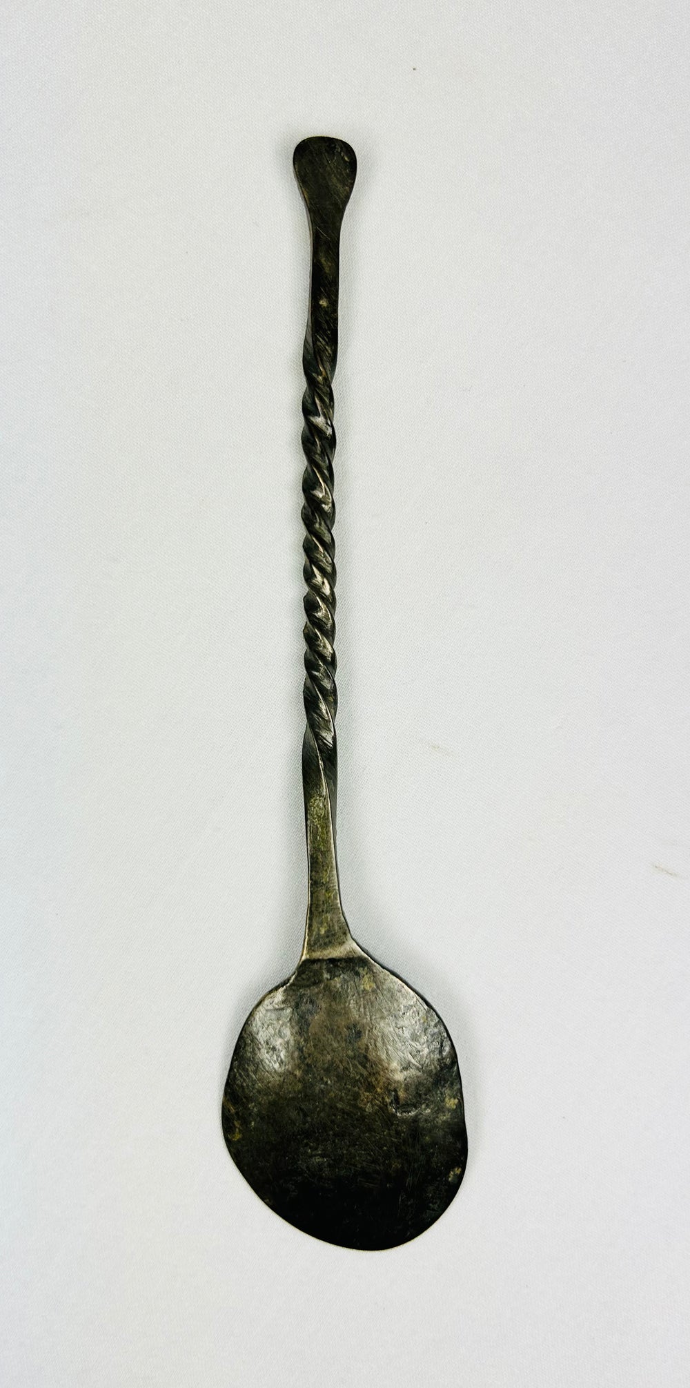 Overhead back view of ancient bronze spoon showing reverse side of bowl, twisted handle, and aged green patina from antiquity.