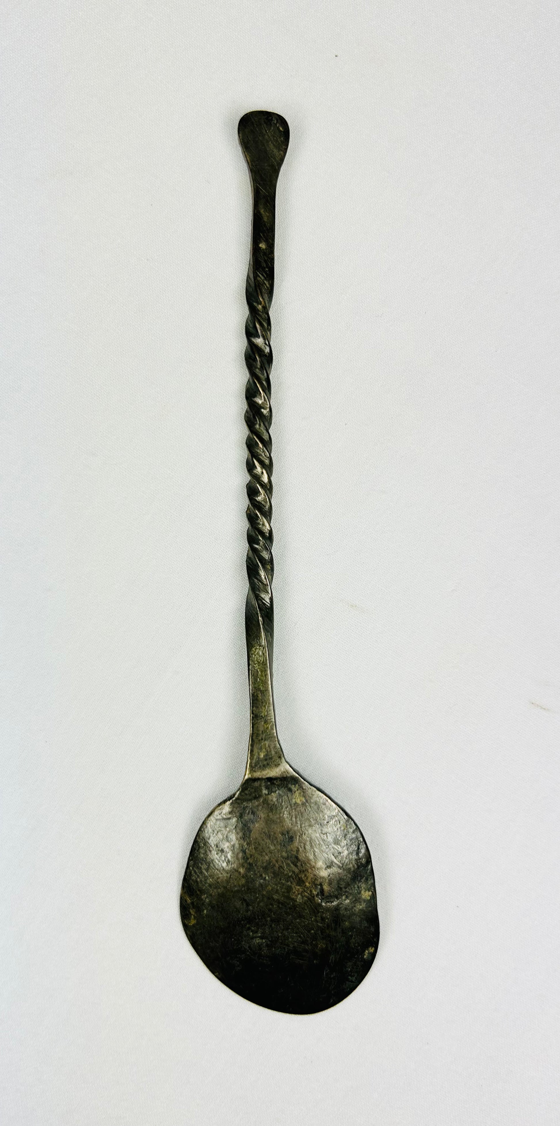 Overhead back view of ancient bronze spoon showing reverse side of bowl, twisted handle, and aged green patina from antiquity.