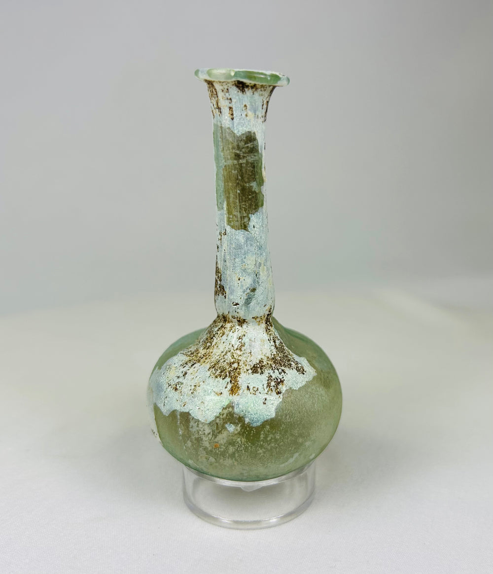 Ancient Roman glass vessel under light showing translucent green tones and mineral surface deposits.