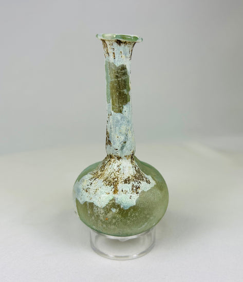 Ancient Roman glass vessel under light showing translucent green tones and mineral surface deposits.
