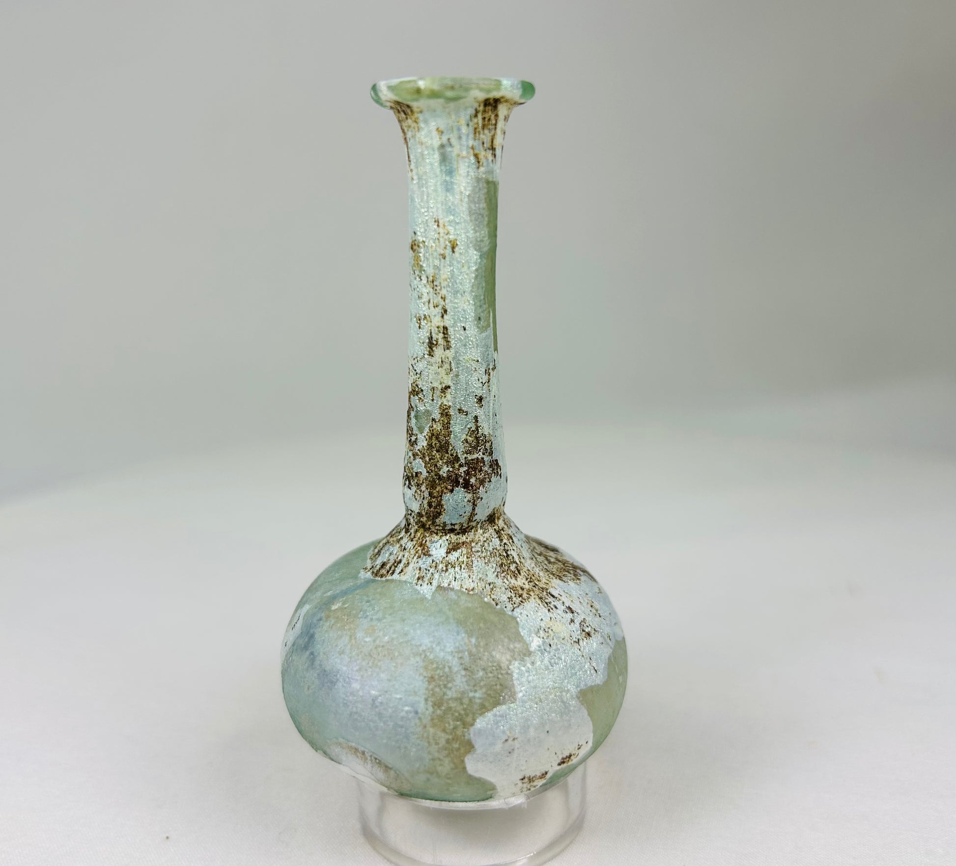 Ancient Roman glass bottle viewed at a soft angle showing natural mineral deposits and patina.