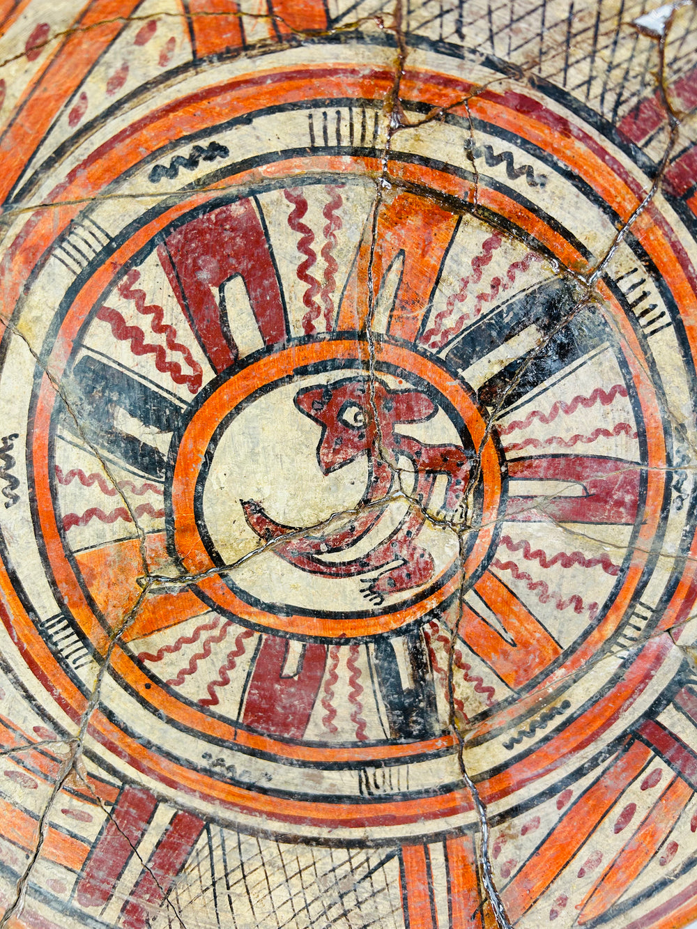 Close-up of zoomorphic center motif on ancient Mesoamerican plate, highlighting fine brushwork and mineral patina.