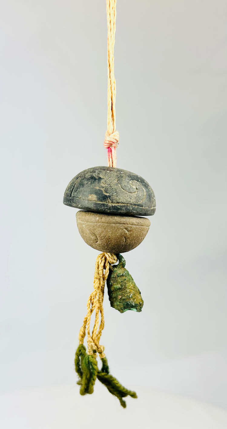Low-angle close-up of ancient bronze bell pendant emphasizing mineral patina and weathering