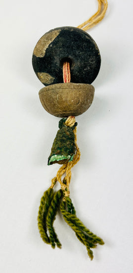 Close-up of ancient bronze bell pendant with original fiber cord and tassel, showing natural verdigris patina and intact upper suspension loop