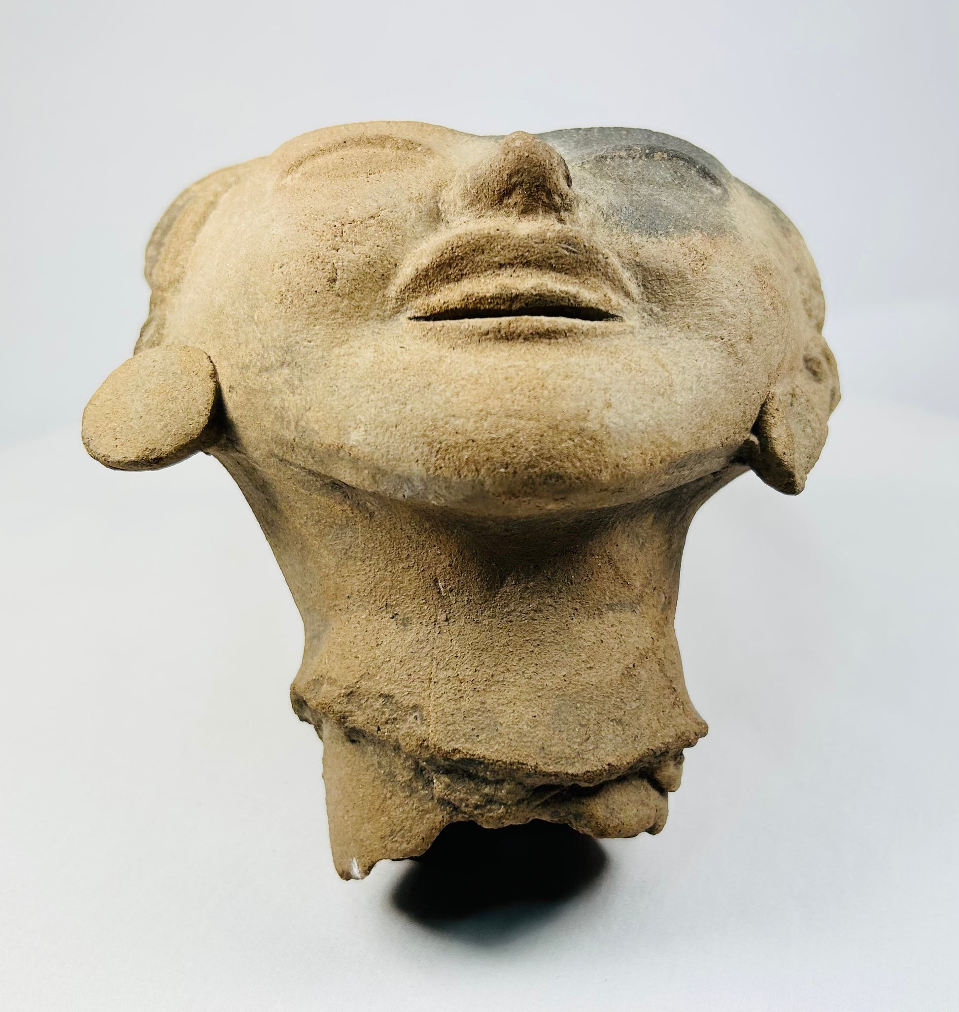 Pre-Columbian terracotta head sculpture viewed from below, showing serene facial expression, detailed lips, and natural clay texture.