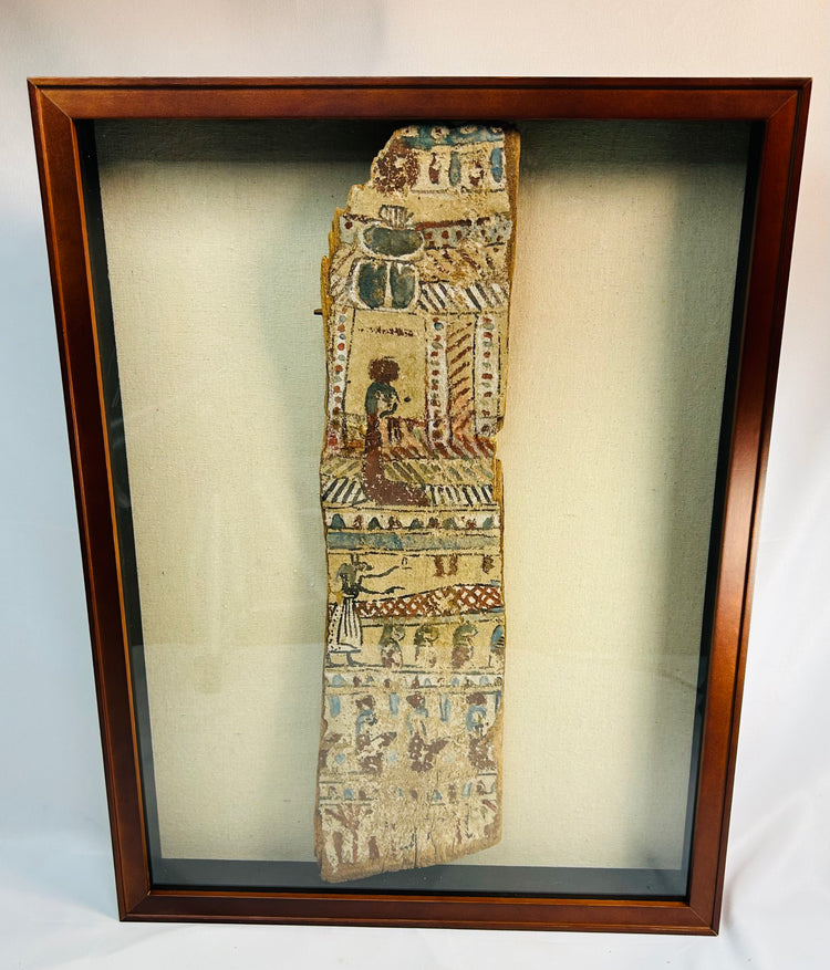 Framed display of ancient Egyptian painted coffin fragment under glass, showing decorative funerary scenes