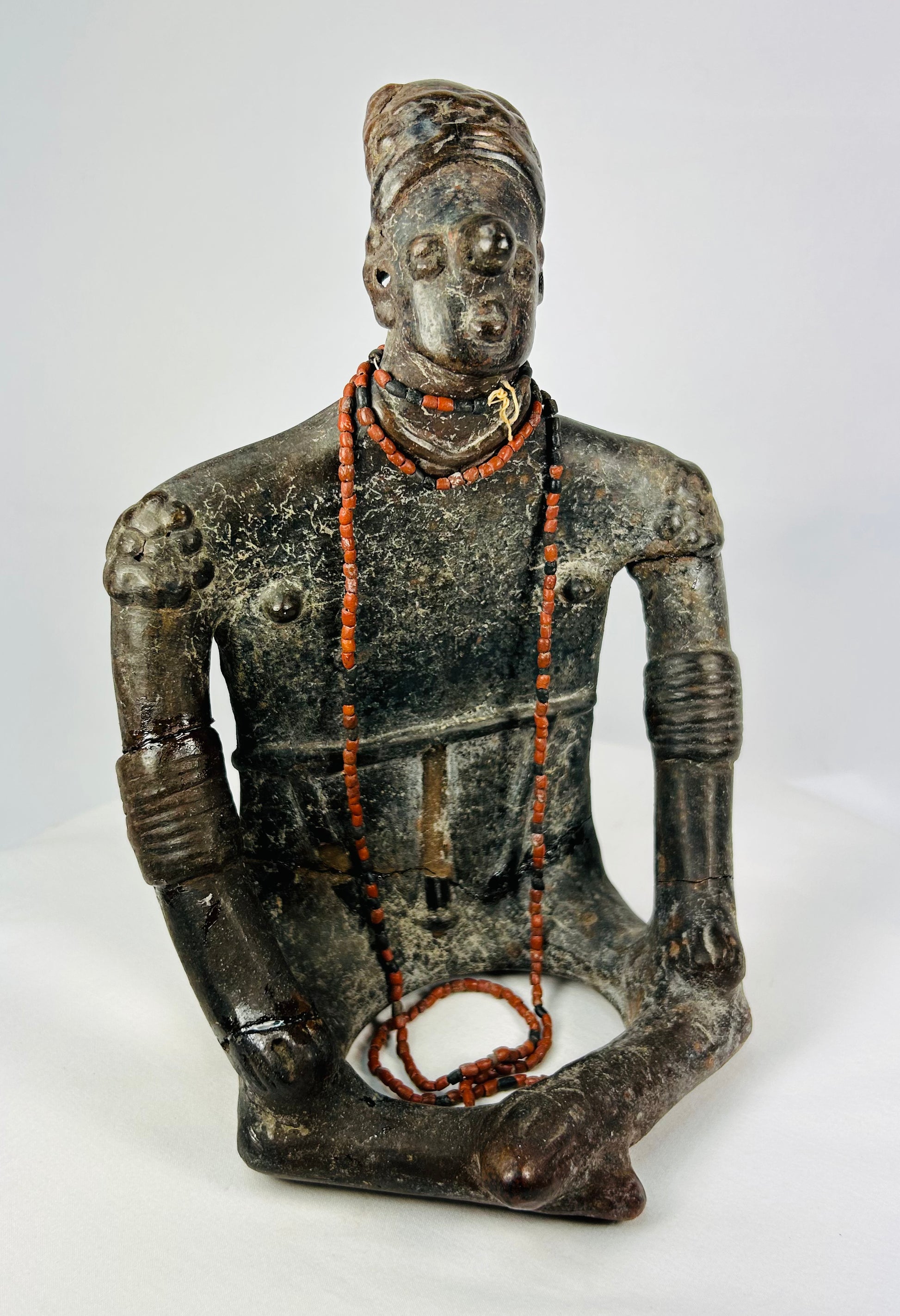 Frontal view of seated Nayarit terracotta effigy with red bead necklaces and elaborate arm bands.