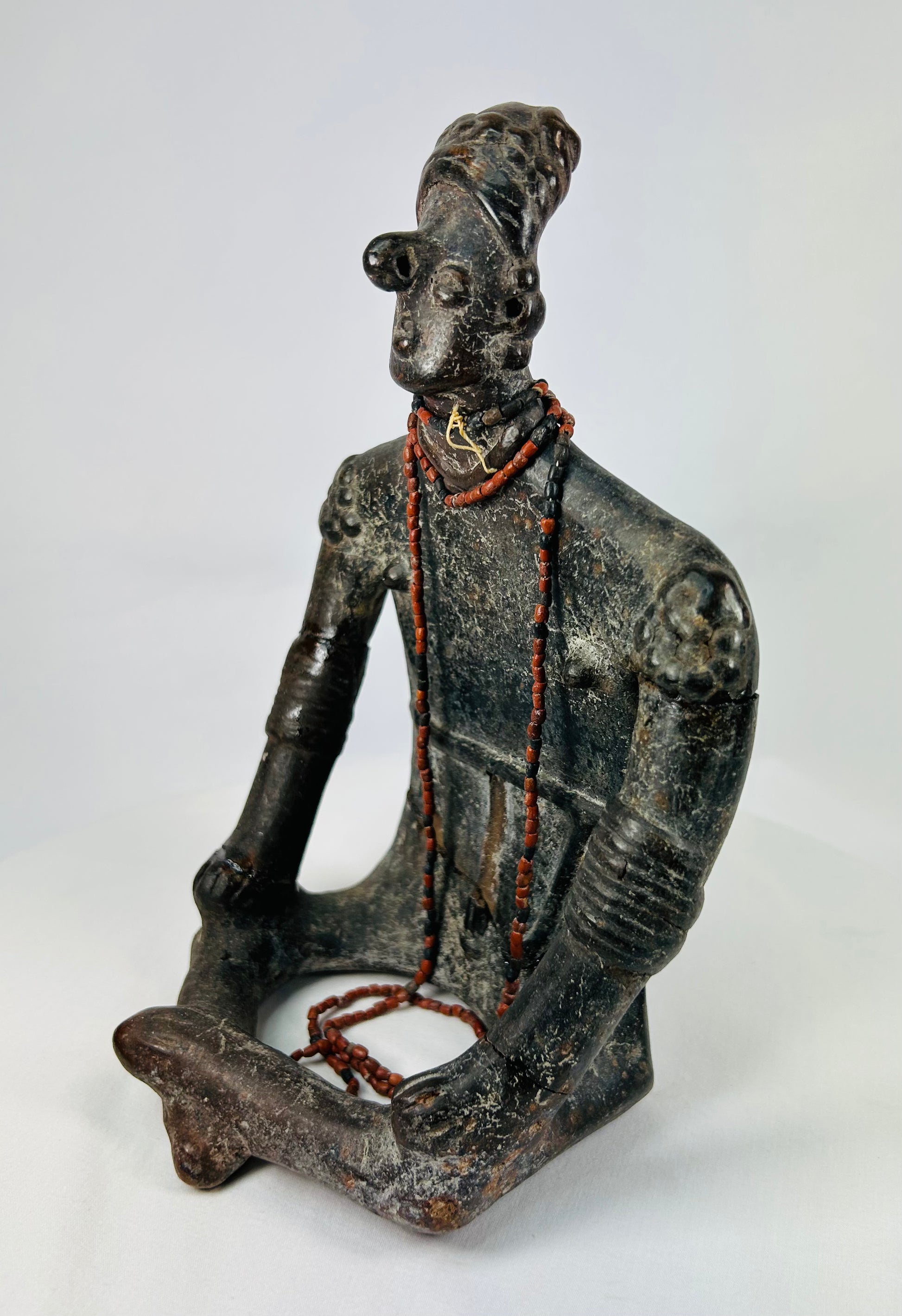 Three-quarter angled view highlighting serene expression, red beads, and cross-legged seated pose.