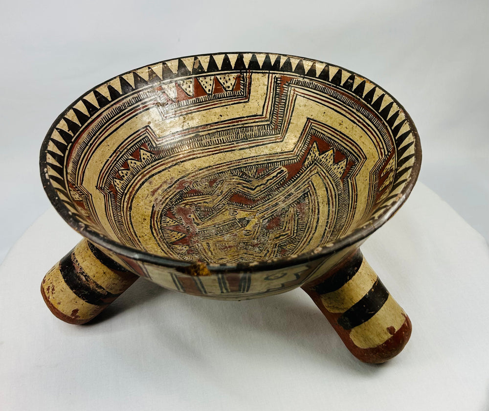 Angled perspective of ancient Costa Rican rattle bowl highlighting three hollow conical legs and cream-red pigments.
