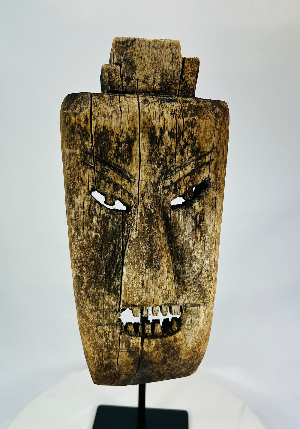 Close-up of facial details on hardwood mask revealing carved teeth, brow ridges, and surface fissures.