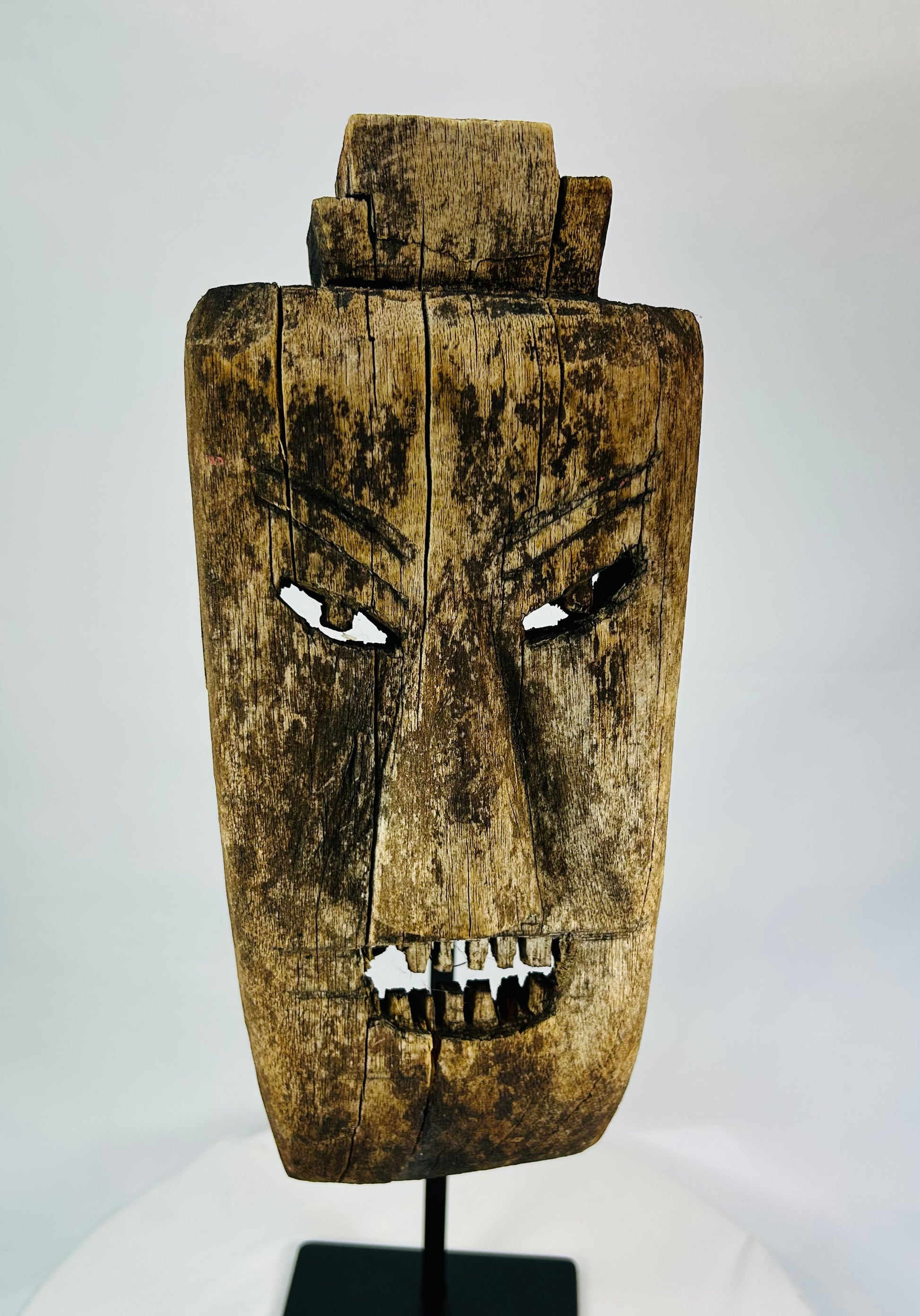 Close-up of facial details on hardwood mask revealing carved teeth, brow ridges, and surface fissures.