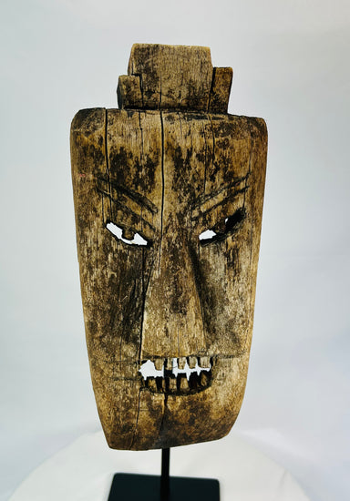 Close-up of facial details on hardwood mask revealing carved teeth, brow ridges, and surface fissures.