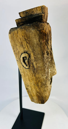 Angled side view of carved tribal mask highlighting expressive grimace, worn patina, and traces of soot from ritual use.