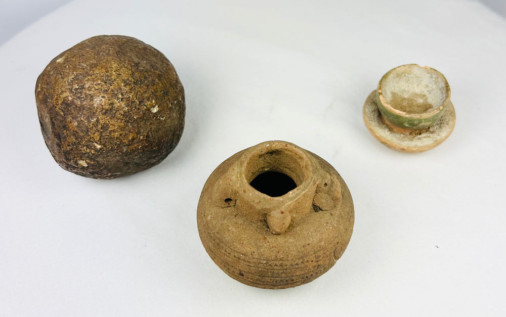 Collection of ancient Asian artifacts including rounded stone object, terracotta oil jar, and pedestal cup with green glaze.