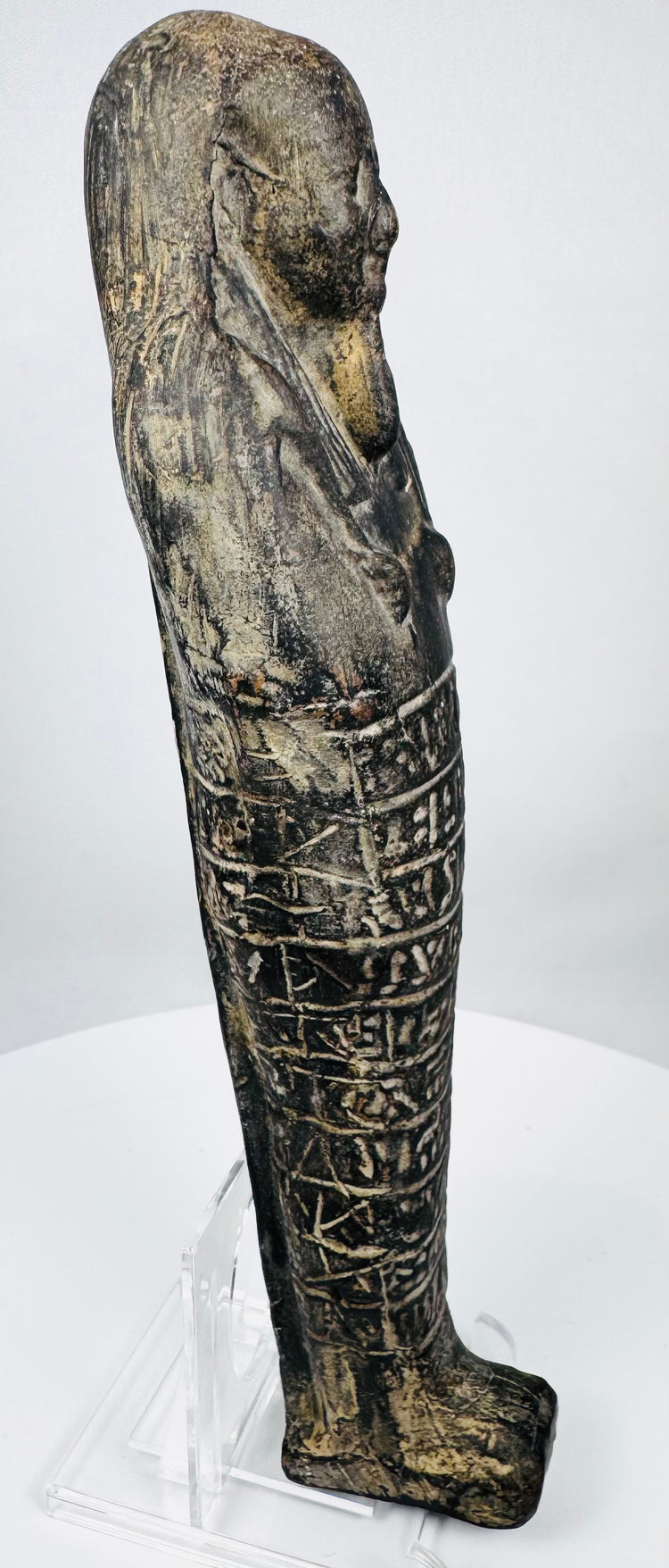 Side view of an ancient Egyptian carved stone ushabti showing its elongated mummiform profile