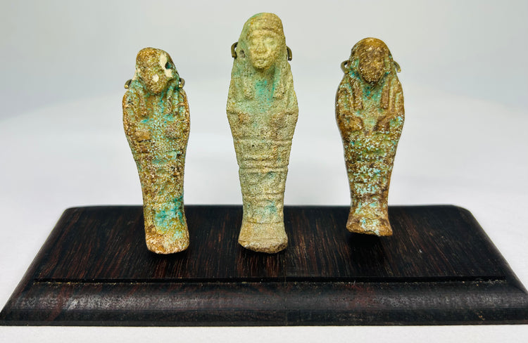 Front view of three ancient Egyptian faience ushabti figures on a dark wooden display stand with mineral-rich turquoise patina.