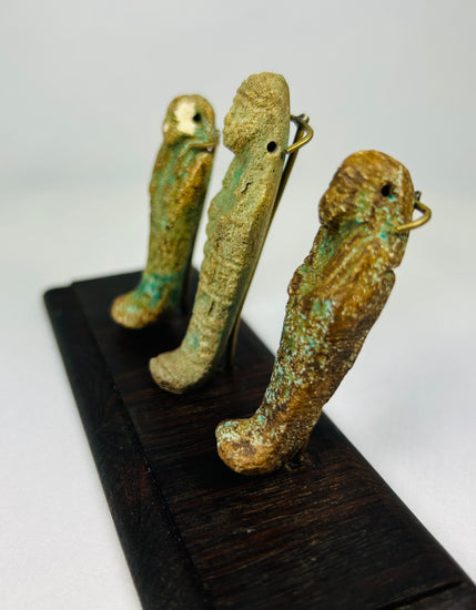 Angled side view of Egyptian faience ushabti trio showing sculptural details and aged green-blue patina on a wooden stand.