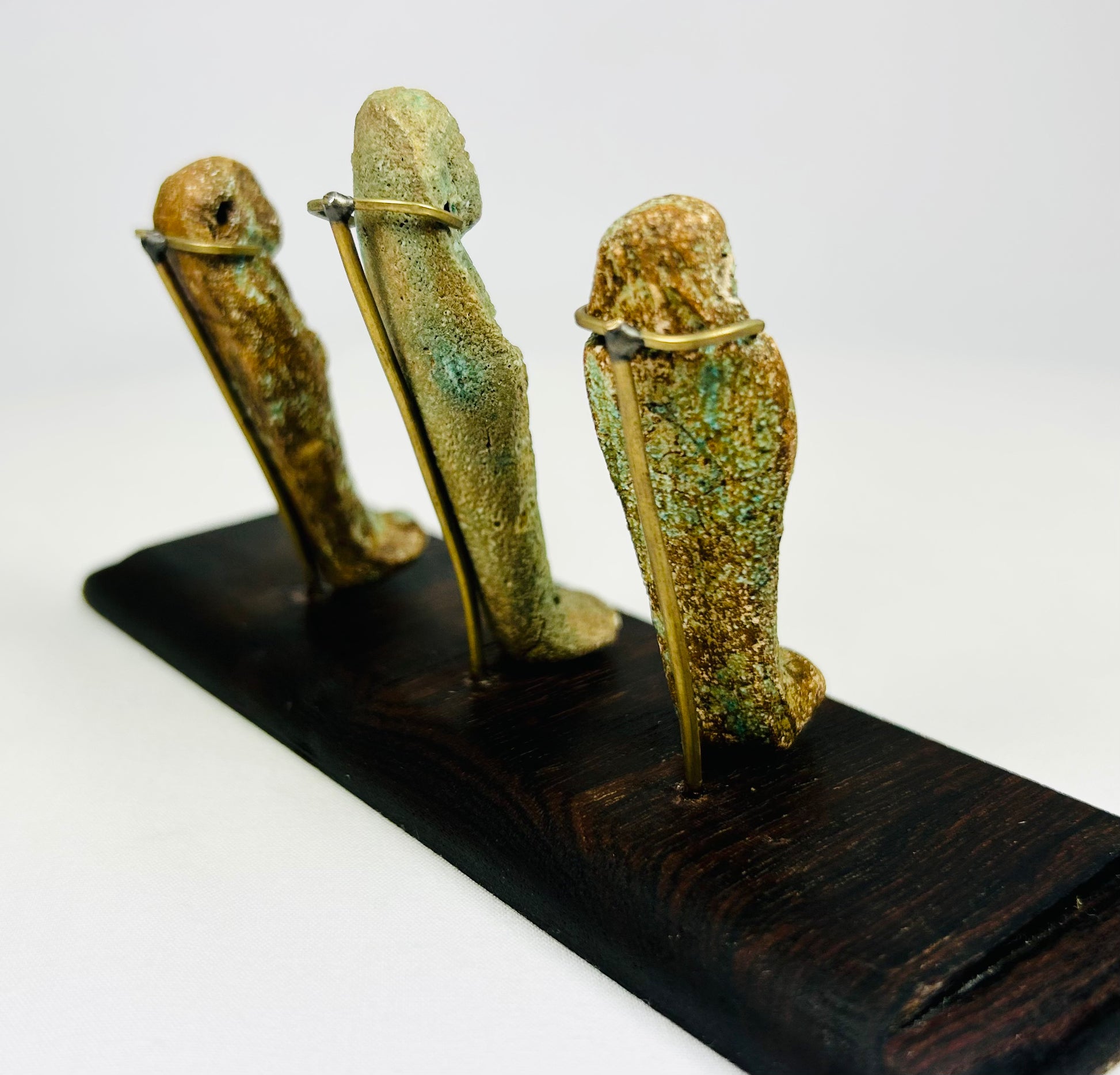 Side perspective of ancient Egyptian ushabti trio highlighting mineral encrustations and faience surfaces on a dark stand.