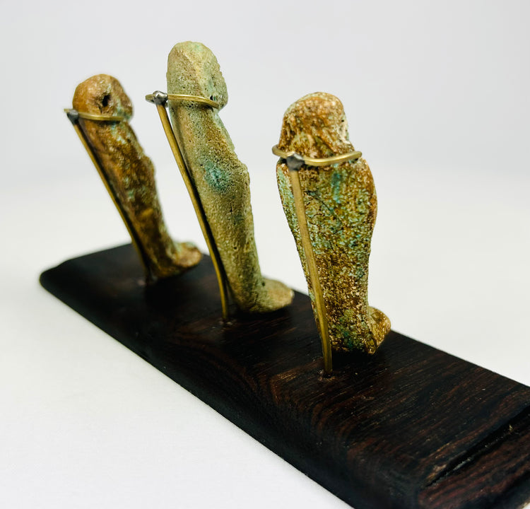 Side perspective of ancient Egyptian ushabti trio highlighting mineral encrustations and faience surfaces on a dark stand.