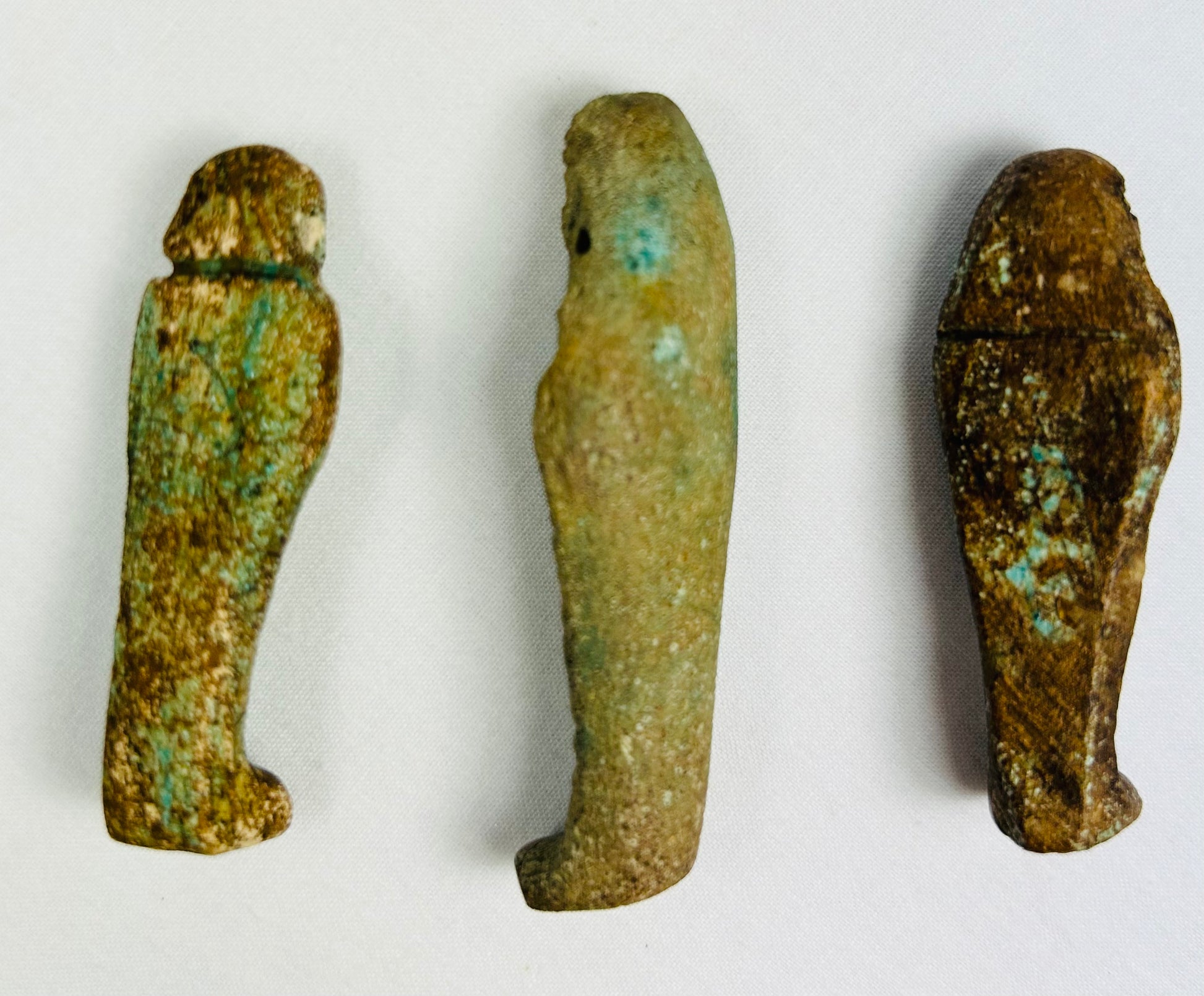 Top-down view of three ancient Egyptian faience ushabti figures showing varying shapes, patina textures, and burial wear.