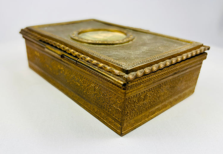 Side view of an antique gold box with intricate floral engravings on a white background.