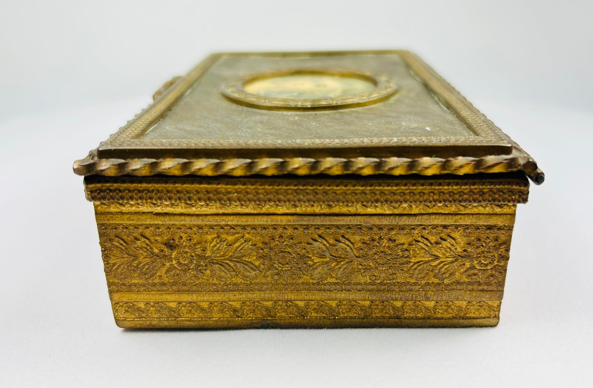 Interior view of an antique gold jewelry box with aged green fabric lining on a white background.