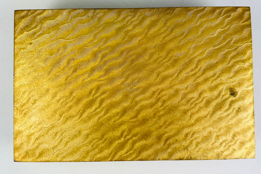 Bottom panel of an antique gold jewelry box showing detailed engraved wavy texture.