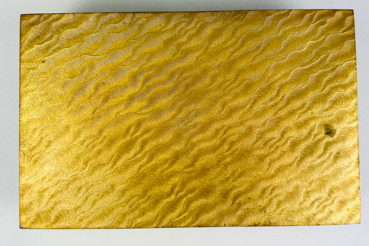 Bottom panel of an antique gold jewelry box showing detailed engraved wavy texture.