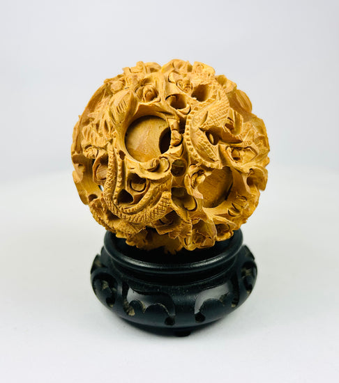 Chinese antique puzzle ball featuring intricate dragon carving on a black wooden stand against a white background.