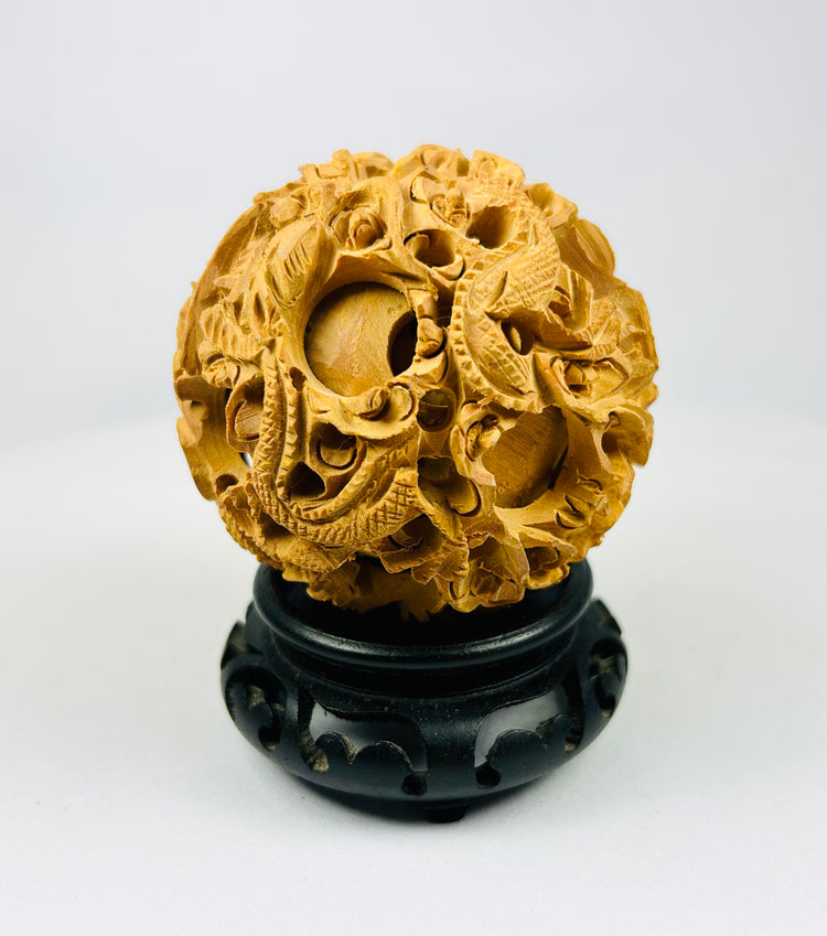 Chinese antique puzzle ball featuring intricate dragon carving on a black wooden stand against a white background.
