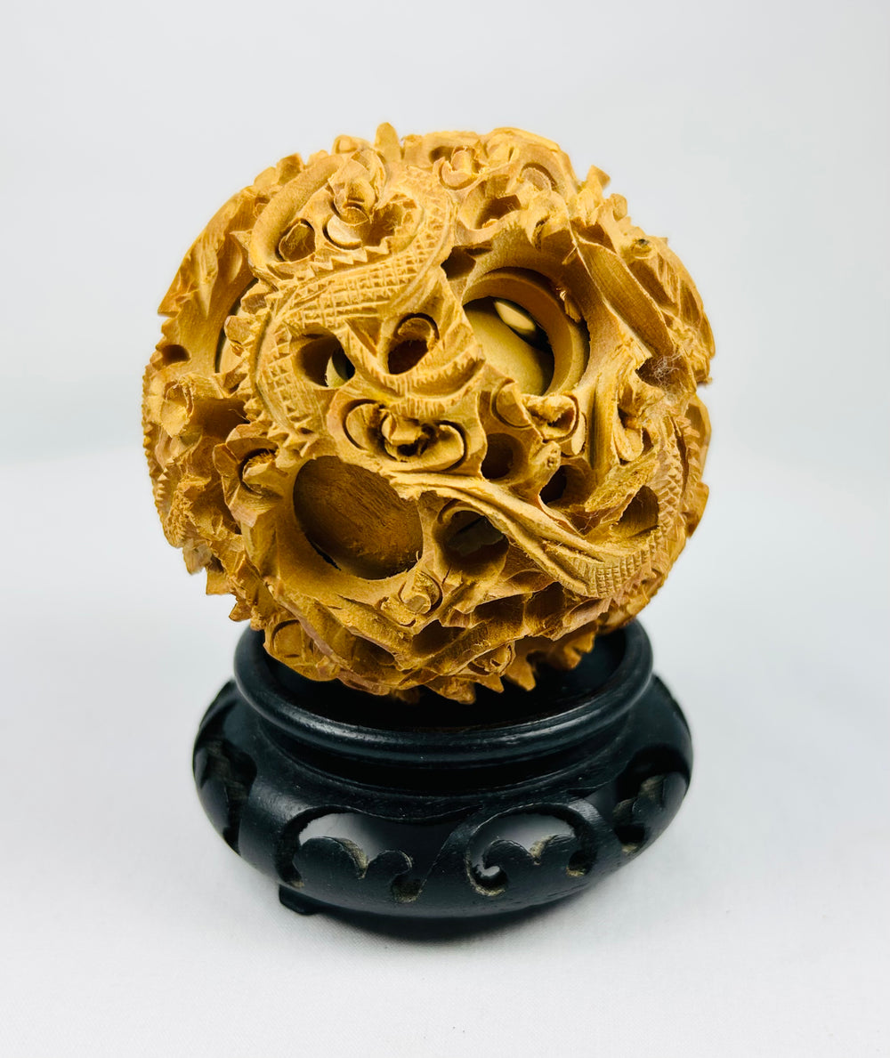 Late Qing Dynasty carved puzzle ball with layered spheres and dragon motifs on a black stand against a white background.