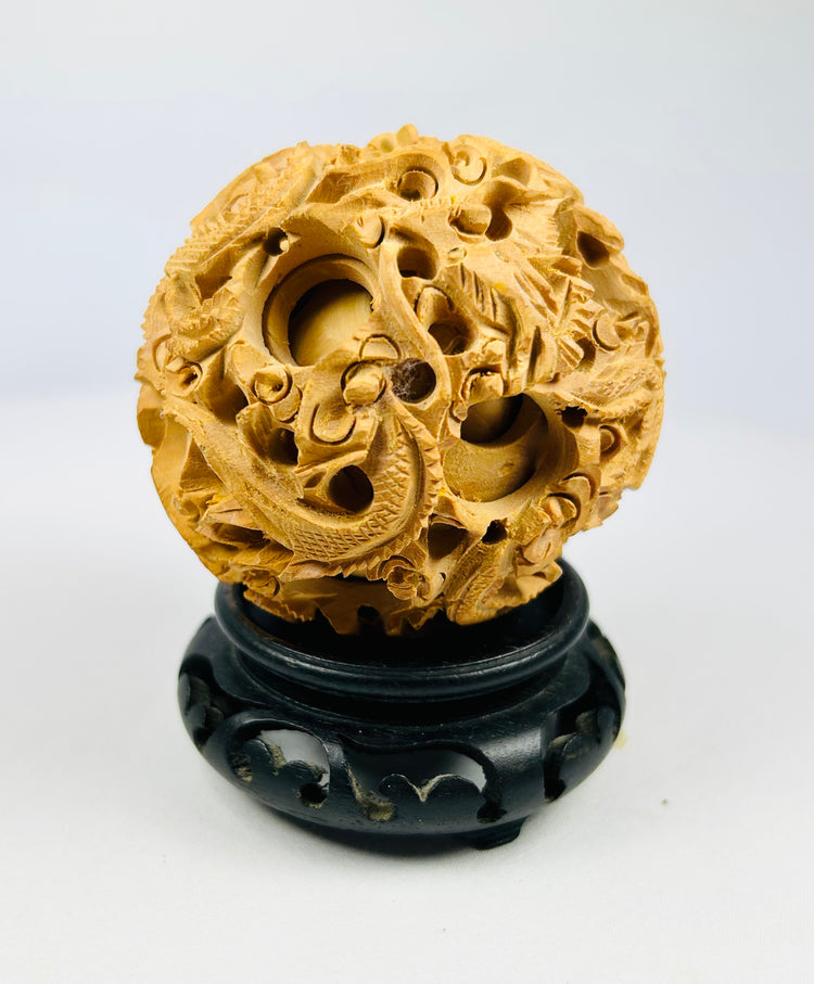 Hand-carved Chinese dragon puzzle ball with pierced latticework displayed on a black wooden stand against a white background.